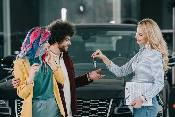 Attractive blonde car dealer giving key to happy man and woman — Stock Photo