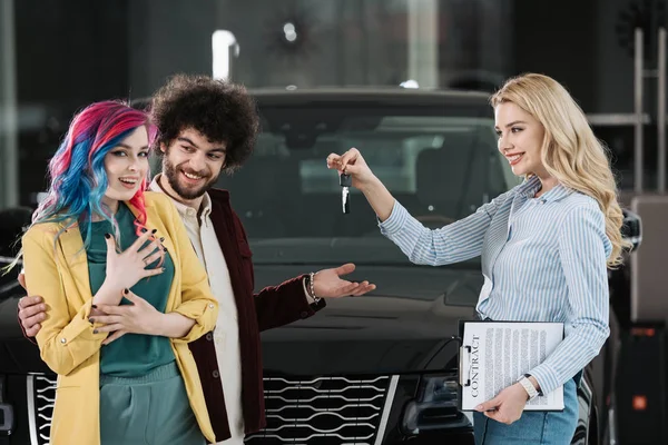 Attrayant concessionnaire de voiture blonde donnant la clé de gai homme et femme — Photo de stock