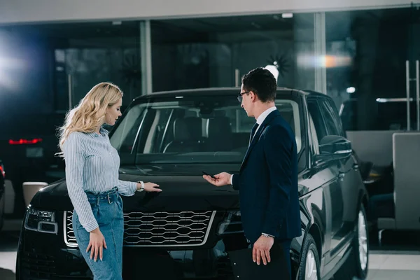 Concesionario de coches que muestra el automóvil a la mujer rubia en sala de exposición de coches - foto de stock