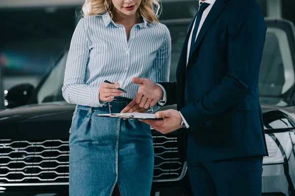 Vista ritagliata del rivenditore di auto in possesso di appunti vicino donna bionda con penna — Foto stock