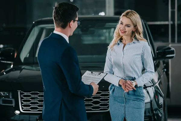 Autohändler hält Klemmbrett mit Vertrag nahe attraktiver blonder Frau — Stockfoto