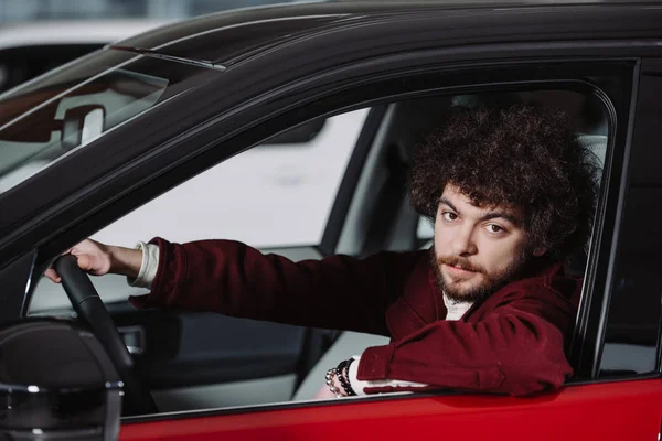 Handsome curly man holding steering wheel while sitting in car — Stock Photo