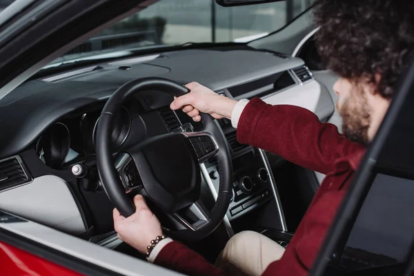 Selektiver Fokus des lockigen Fahrers, der das Lenkrad hält, während er im Auto sitzt — Stockfoto