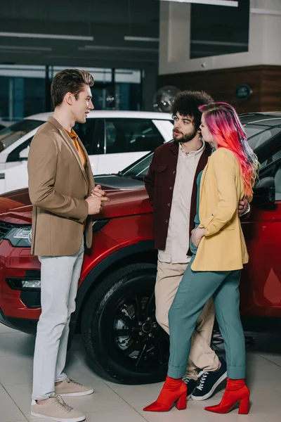 Schöner Mann im Gespräch mit Freunden in der Nähe von Autos im Autohaus — Stockfoto