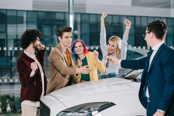 Car dealer giving key to happy friends standing near white car — Stock Photo