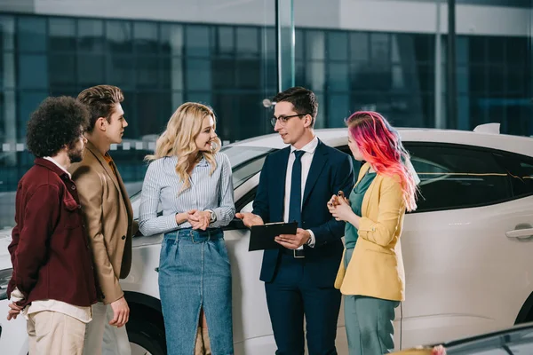 Handsome car dealer holding clipboard and taking with group of friends — Stock Photo