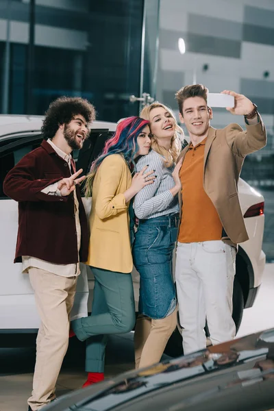 Alegre grupo de amigos tomando selfie cerca de coche blanco - foto de stock