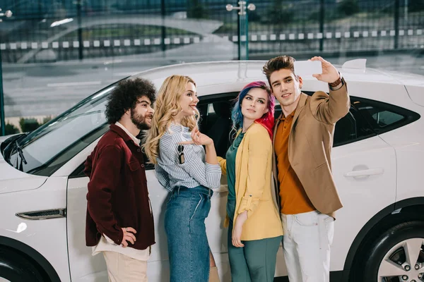 Heureux groupe d'amis prenant selfie sur smartphone près de voiture blanche — Photo de stock