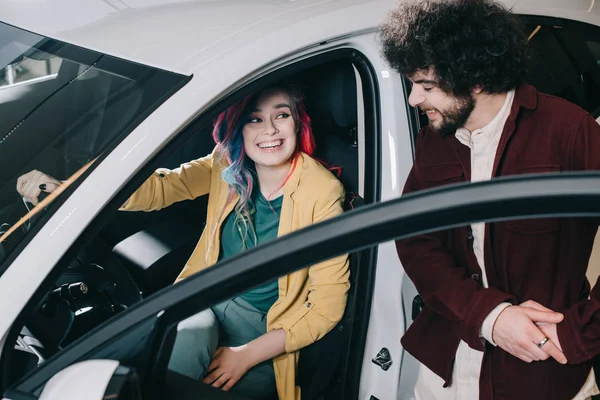 Vista aerea della ragazza allegra con i capelli colorati seduti in auto e guardando l'uomo riccio — Foto stock