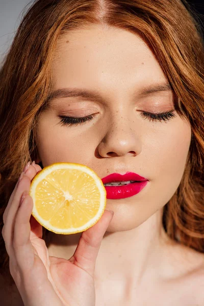 Beautiful sensual redhead girl with red lips and eyes closed posing with cut lemon — Stock Photo