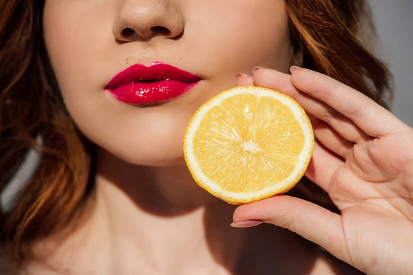 Обрізаний вид рудої дівчини з червоними губами позує з лимоном — стокове фото