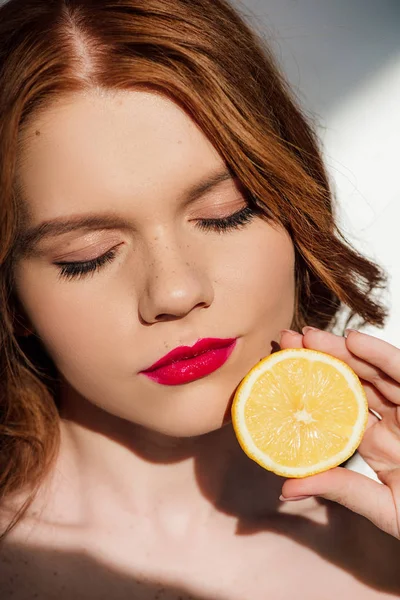 Beautiful sensual redhead girl with red lips and eyes closed posing with lemon — Stock Photo