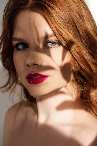 Belle jeune femme rousse avec des lèvres rouges et ombre sur le visage regardant la caméra — Photo de stock