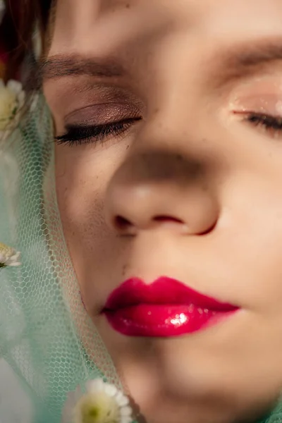 Vista de cerca de la hermosa joven con los ojos cerrados y los labios rojos cubiertos de velo con flores - foto de stock