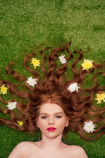 Vista superior da bela jovem ruiva com lábios vermelhos e flores de crisântemo no cabelo na grama — Fotografia de Stock