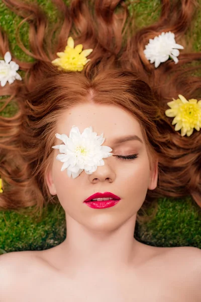 Вид зверху красива молода руда жінка з червоними губами та квітами хризантем у волоссі на траві — стокове фото