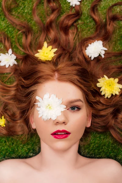 Vista superior de la hermosa mujer joven con labios rojos y flores de crisantemo en el pelo en la hierba - foto de stock