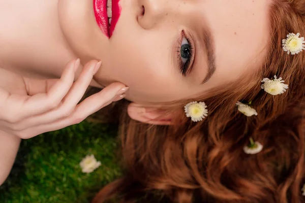 Vista recortada de hermosa joven pelirroja con labios rojos y flores de crisantemo en el pelo - foto de stock