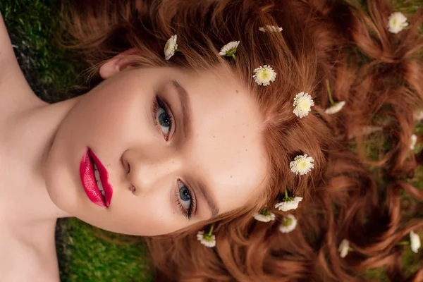 Schöne junge rothaarige Frau mit roten Lippen und Chrysanthemenblüten im Haar, die in die Kamera schaut — Stockfoto
