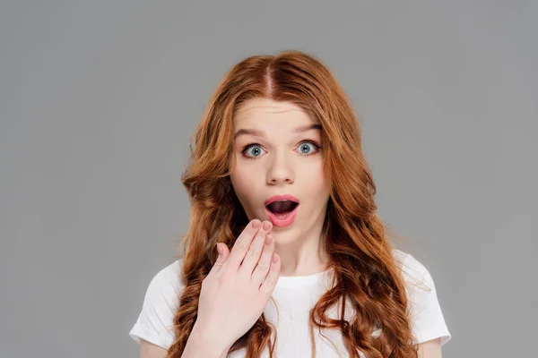 Shocked redhead girl gesturing with hand and looking at camera isolated on grey — Stock Photo