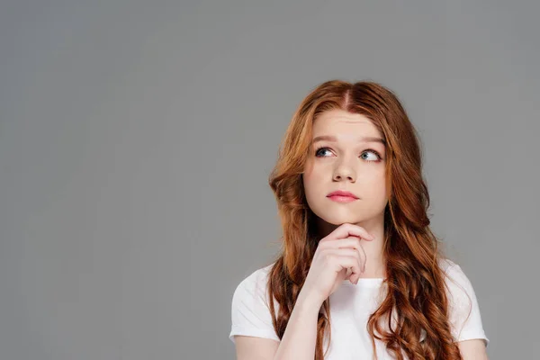 Thoughtful redhead girl propping chin with hand isolated on grey with copy space — Stock Photo