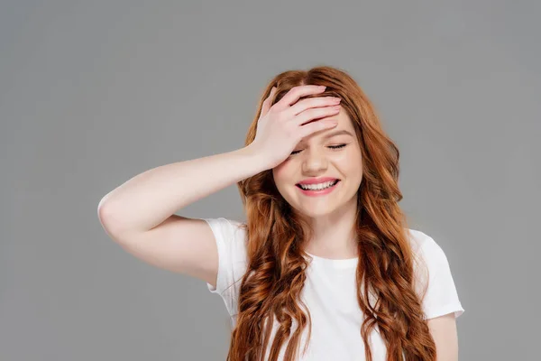 Beautiful redhead girl in white t-shirt touching forehead and smiling isolated on grey — Stock Photo