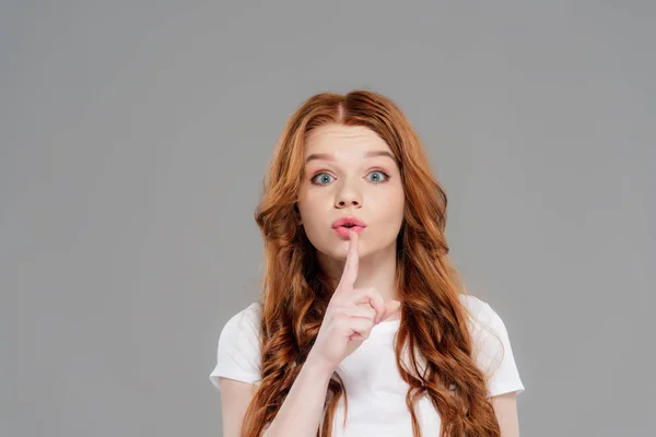 Beautiful redhead girl looking at camera and doing silent gesture isolated on grey — Stock Photo