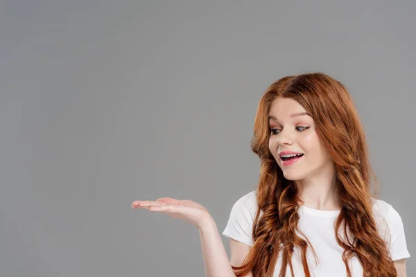 Beautiful redhead girl gesturing with hand and presenting something isolated on grey with copy space — Stock Photo