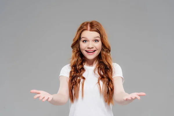 Surprised redhead girl with outstretched hands looking at camera and smiling isolated on grey — Stock Photo