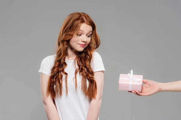 Beautiful redhead girl looking at pink gift box isolated on grey — Stock Photo