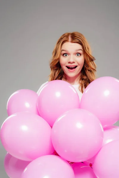 Beautiful surprised girl with pink air balloons looking at camera isolated on grey — Stock Photo