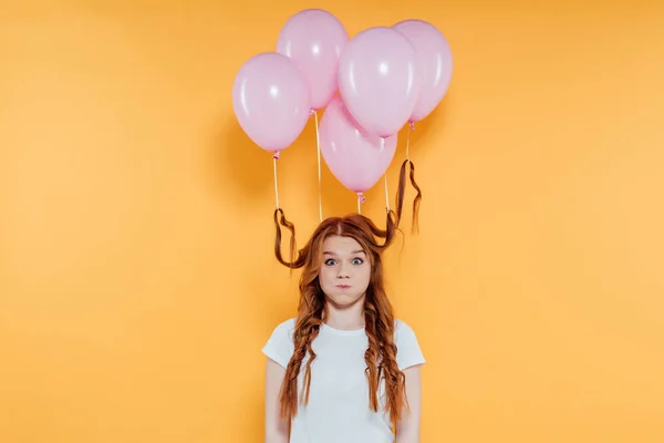 Rothaariges Mädchen mit Luftballons an den Haaren, die Wangen wehen lassen und die Kamera isoliert auf gelb betrachtet — Stockfoto