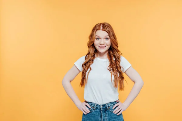 Belle rousse fille avec mains akimbo regarder caméra et posant isolé sur jaune — Photo de stock