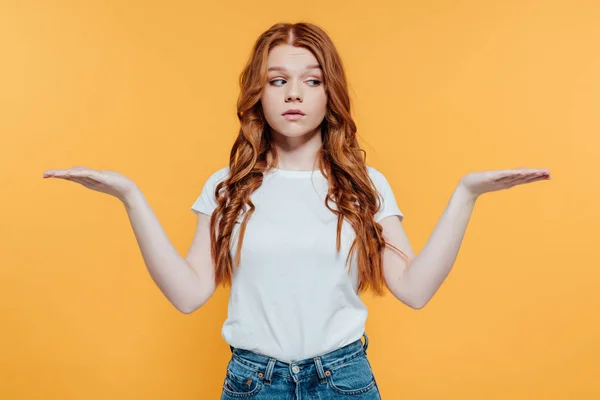 Beautiful redhead girl showing shrug gesture isolated on yellow — Stock Photo