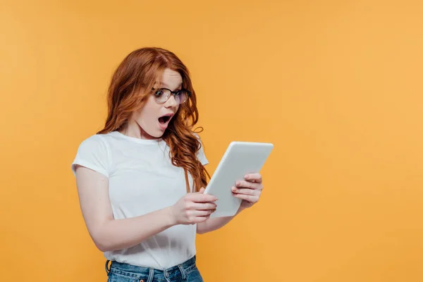 Surprised redhead girl using digital tablet isolated on yellow with copy space — Stock Photo