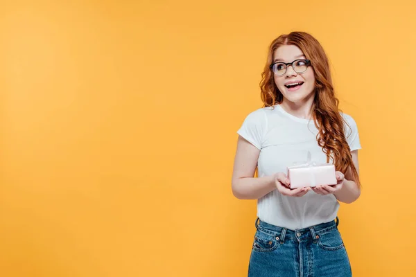 Schön überrascht rothaarige Mädchen halten Geschenkbox isoliert auf gelb mit Kopierraum — Stockfoto