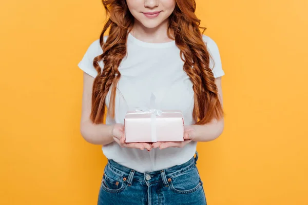 Abgeschnittene Ansicht des lächelnden rothaarigen Mädchens mit Geschenkbox isoliert auf gelb — Stockfoto