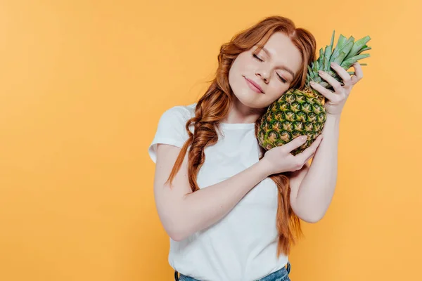 Beautiful redhead girl with eyes closed posing with pineapple isolated on yellow with copy space — Stock Photo