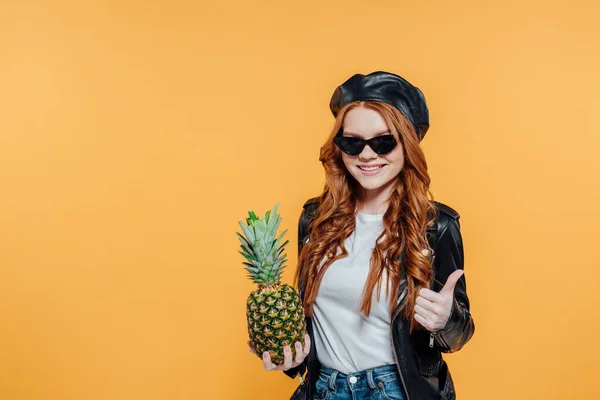 Redhead girl in leather jacket with pineapple smiling and showing thumb up isolated on yellow with copy space — Stock Photo