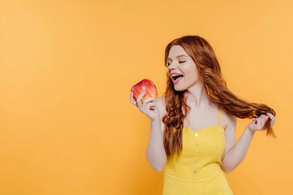 Beautiful redhead girl biting apple isolated on yellow with copy space — Stock Photo