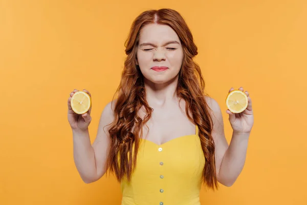 Menina ruiva segurando limões e fazendo expressão facial isolado no amarelo — Fotografia de Stock