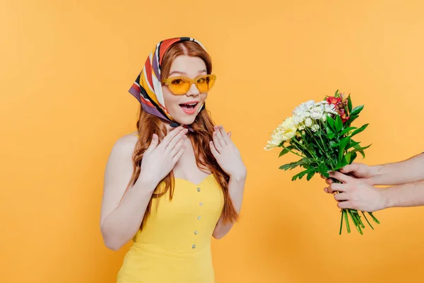 Überrascht Mädchen mit Kopftuch und Sonnenbrille gestikuliert, während Mann mit Blumen in der Hand isoliert auf gelb — Stockfoto