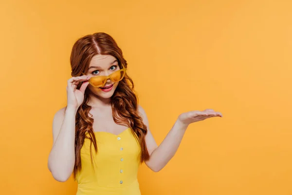 Beautiful redhead girl gesturing with hand and presenting something isolated on yellow with copy space — Stock Photo