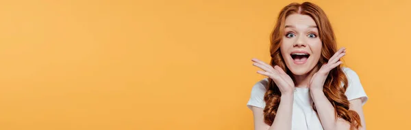 Panoramic shot of beautiful excited redhead girl looking at camera and gesturing with hands isolated on yellow — Stock Photo