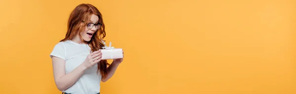 Plano panorámico de chica pelirroja excitada sosteniendo caja de regalo aislada en amarillo con espacio de copia - foto de stock
