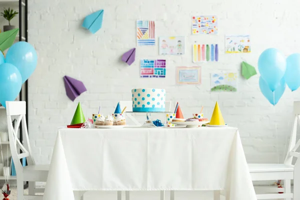 Bolo festivo e bonés de festa na mesa no quarto decorado para festa de aniversário com balões de ar — Fotografia de Stock