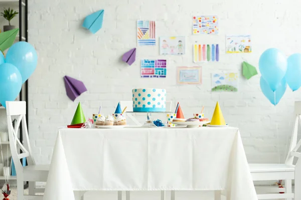 Festive cake and party caps on table in room decorated for birthday party with air balloons — Stock Photo