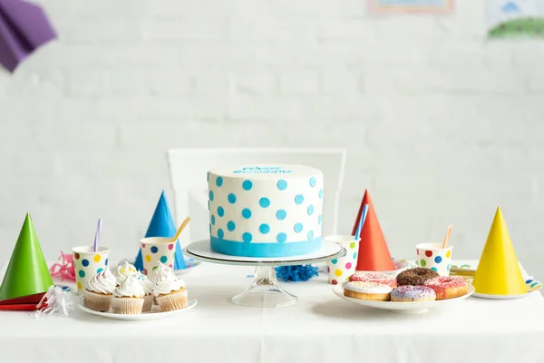 Delicious birthday cake with cupcakes, doughnuts and paper cups on festive table — Stock Photo
