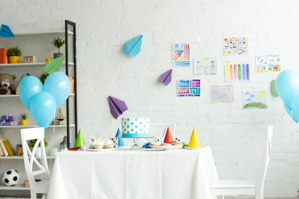 Gâteau festif et casquettes de fête sur la table dans la chambre décorée pour la fête d'anniversaire avec des ballons à air — Photo de stock