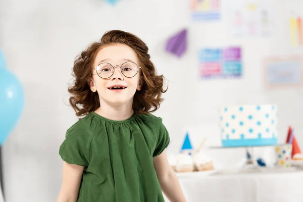Adorable kid in glasses looking at camera and smiling during birthday celebration at home — Stock Photo